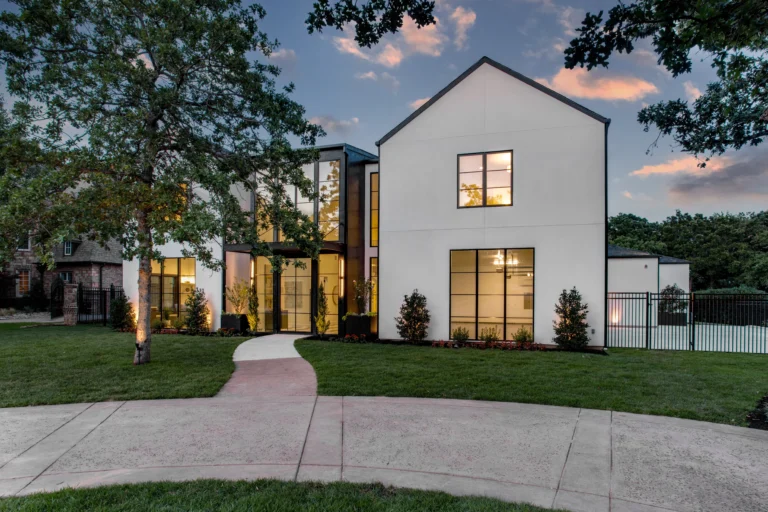 Modern white two-story luxury home with large windows, landscaped yard, and curved walkway at sunset